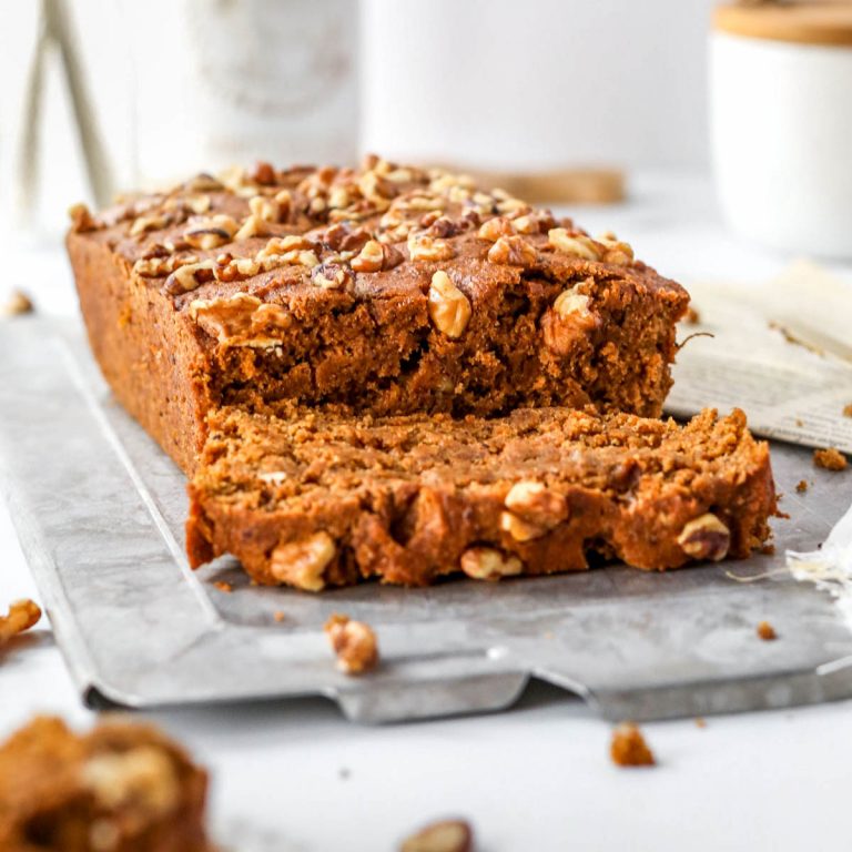 vegan pumpkin bread sitting on a gray tray with walnuts on top of the bread.