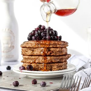 a stack of oat flour pancakes with blueberries and a drizzle of maple syrup