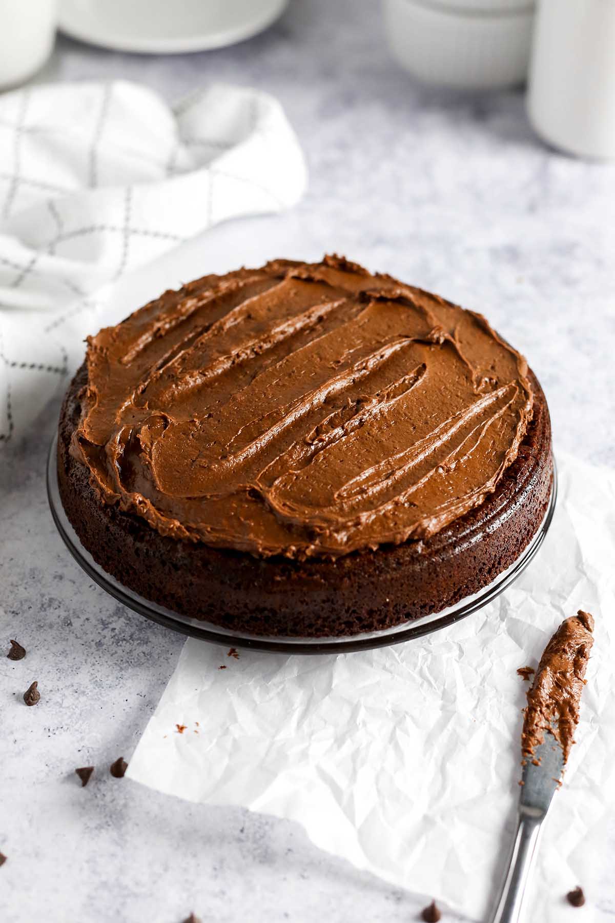 a chocolate cake on a clear glass plate with chocolate frosting spread on top