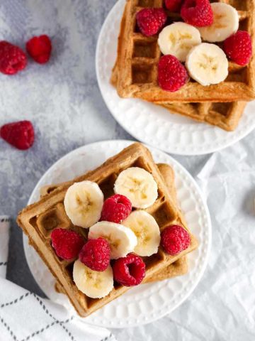 two plates of dairy free waffles with bananas and raspberries on top