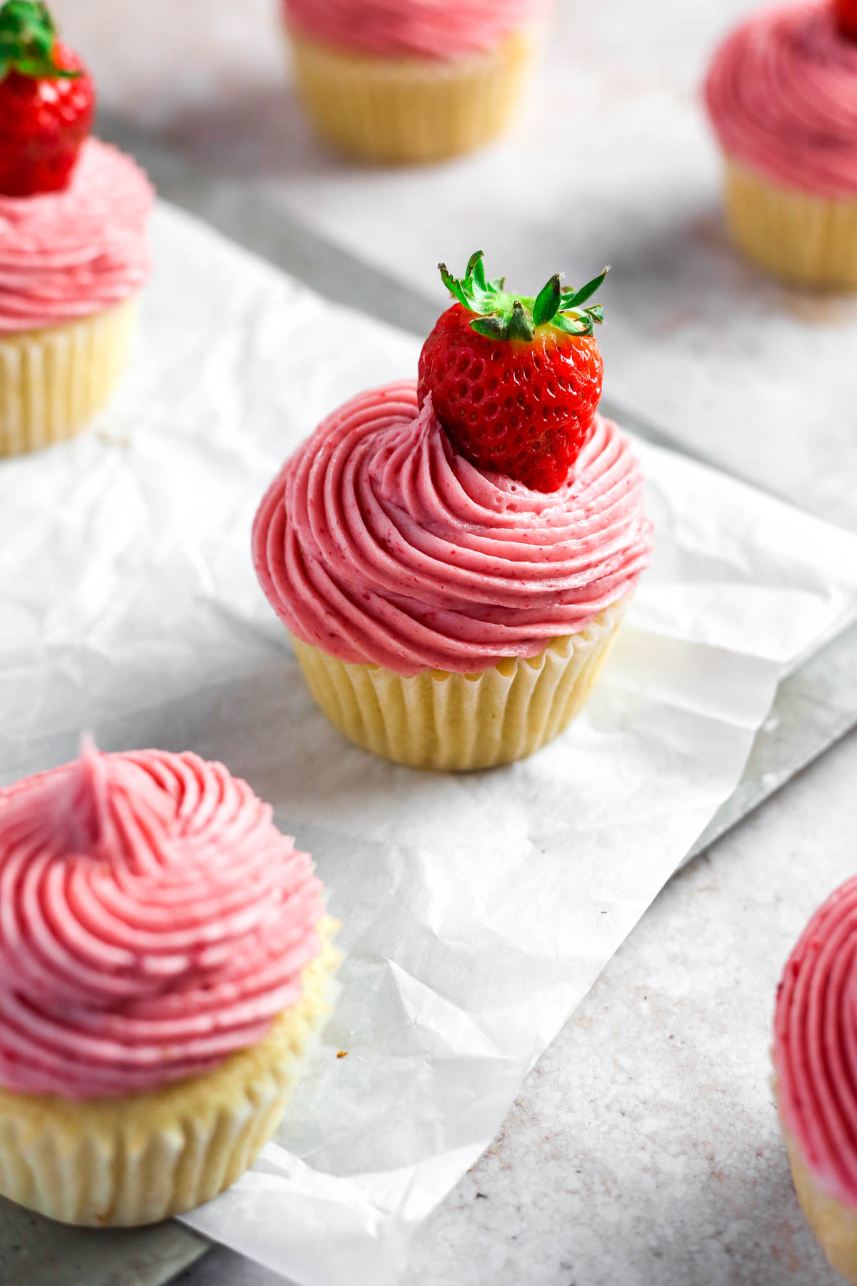 a strawberry filled cupcake on parchment paper, with perfectly piped frosting on top and a juicy strawberry on top.