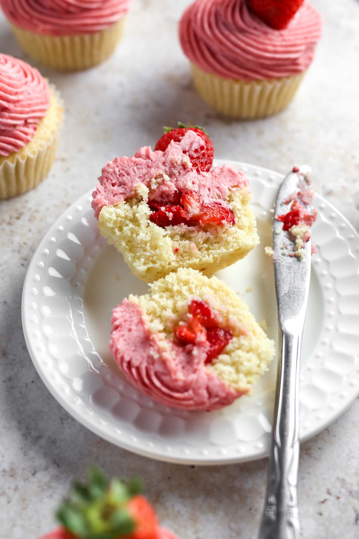 a strawberry filled cupcake sliced in half on a white dessert plate, showing the strawberry filling inside.