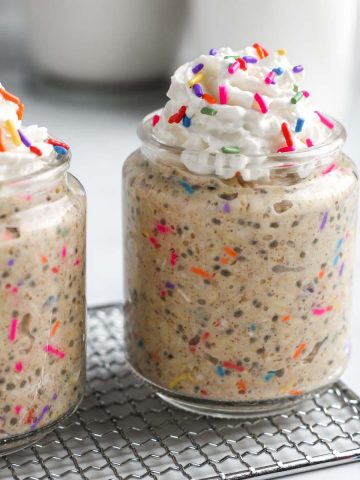 two jars of birthday cake overnight oats with coconut whipped cream and rainbow sprinkles.