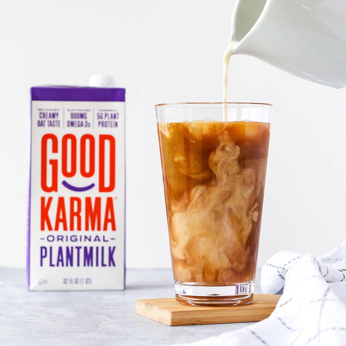 pouring almond milk into a glass of coffee, with good karma foods product in the background.