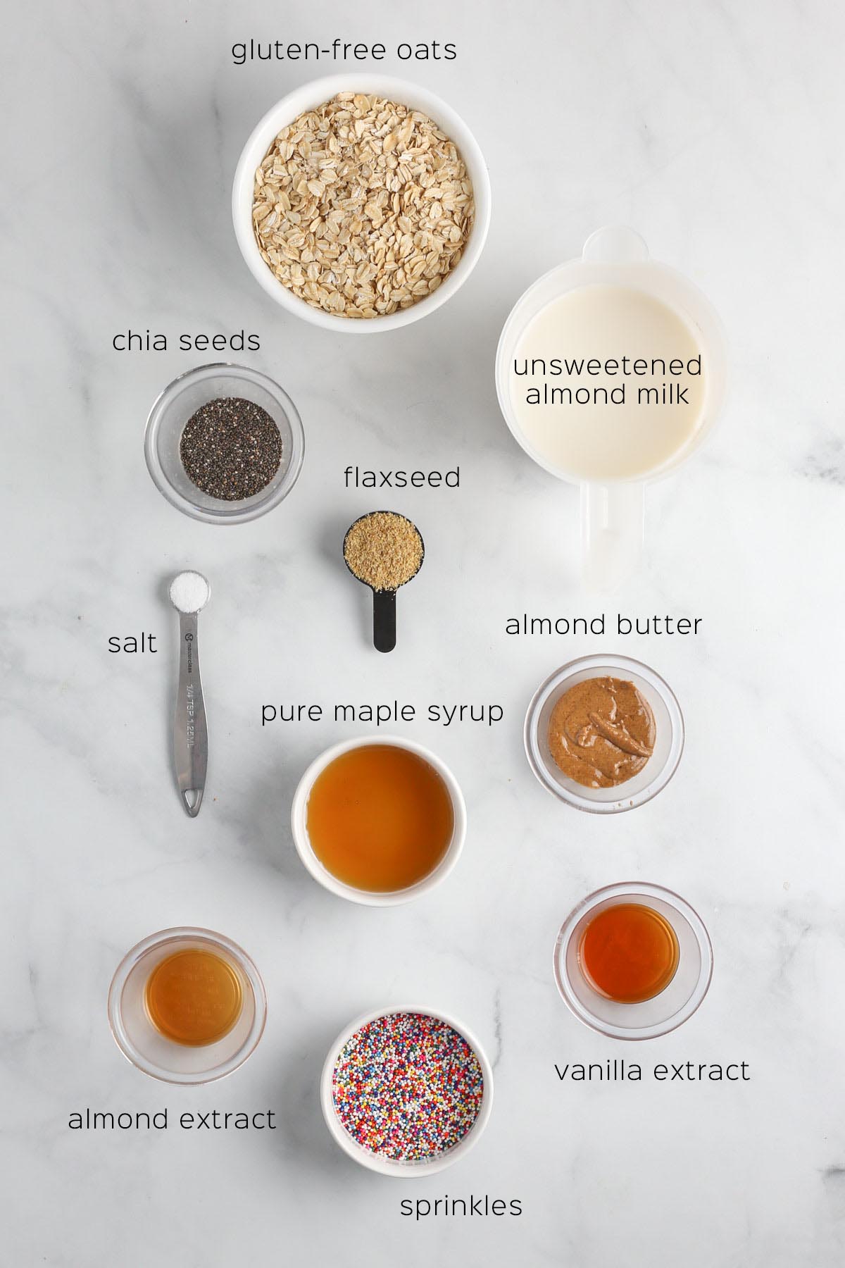 all ingredients to make the overnight oats placed in small white dishes on a marble surface.