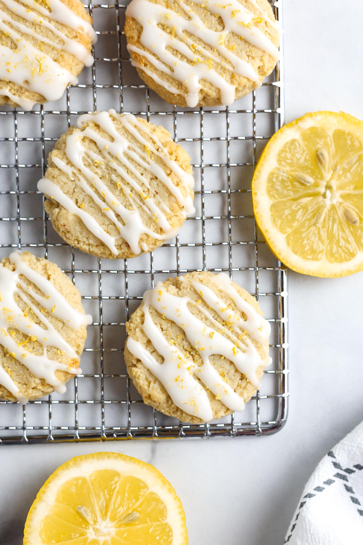 vegan lemon cookies with a drizzle of lemon glaze and lemon zest on top. The cookies are on a gray tray.