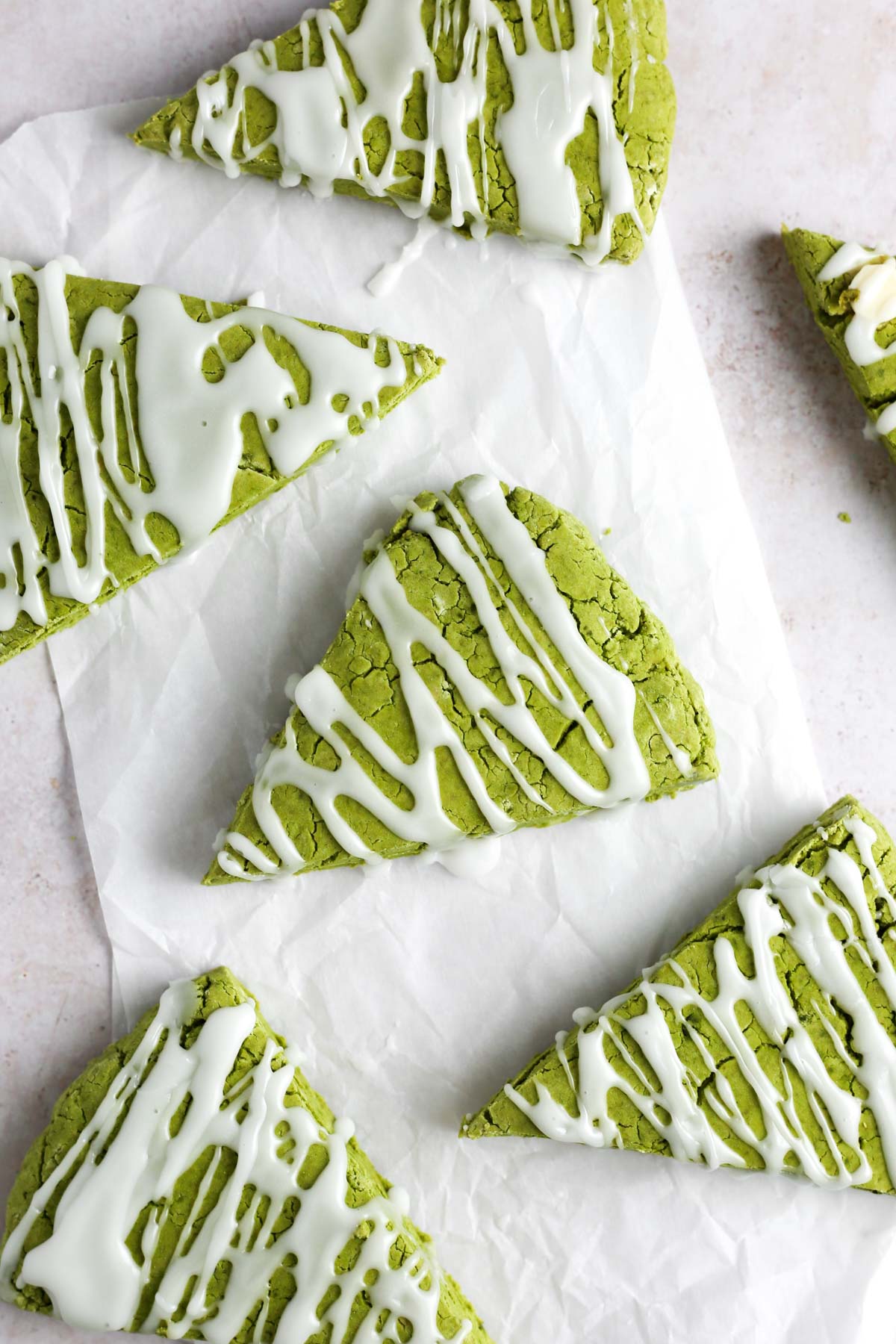 multiple green matcha scones on parchment paper, topped with vanilla glaze.