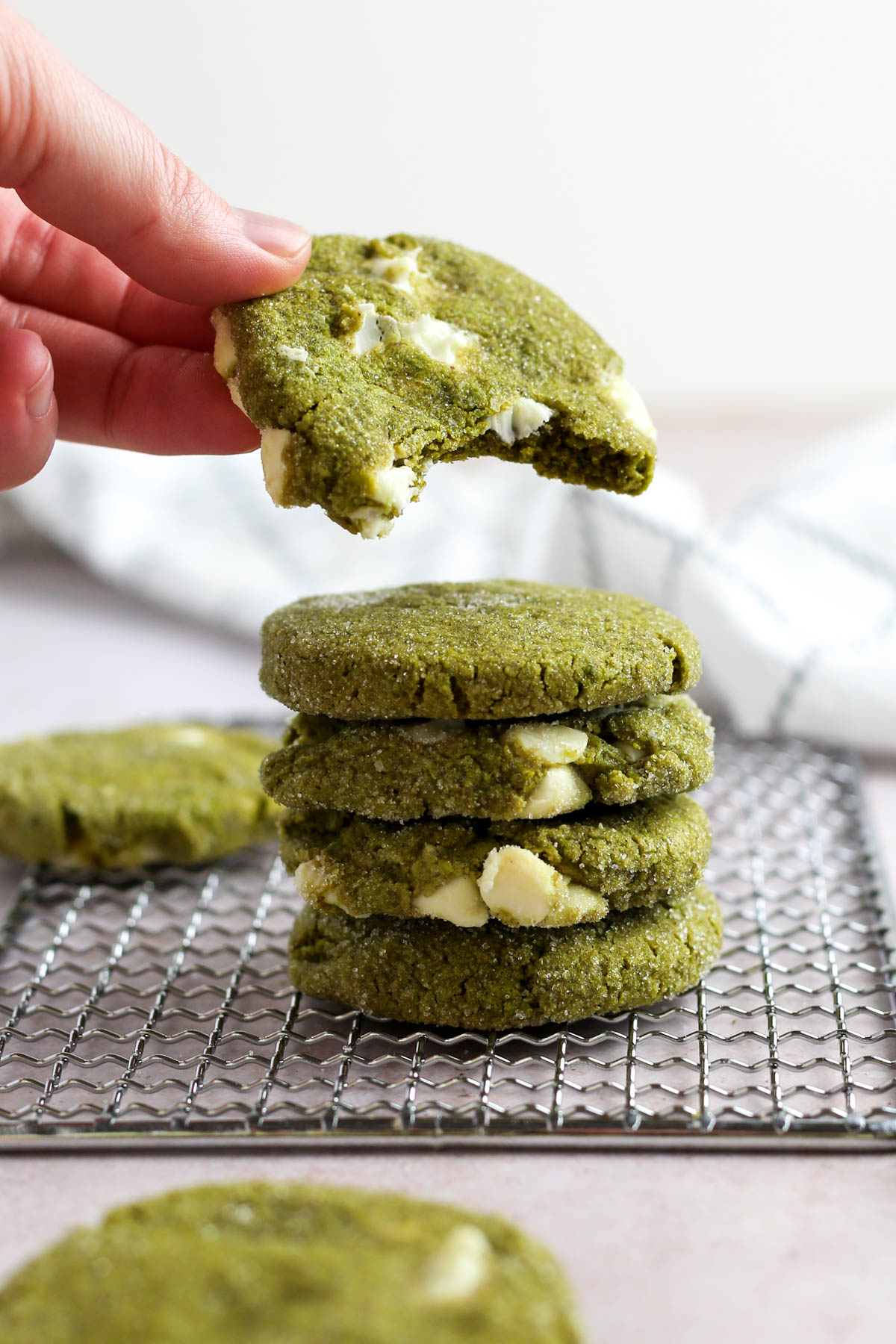 a stack of five matcha cookies, with the top cookie being picked up by someone's hand.