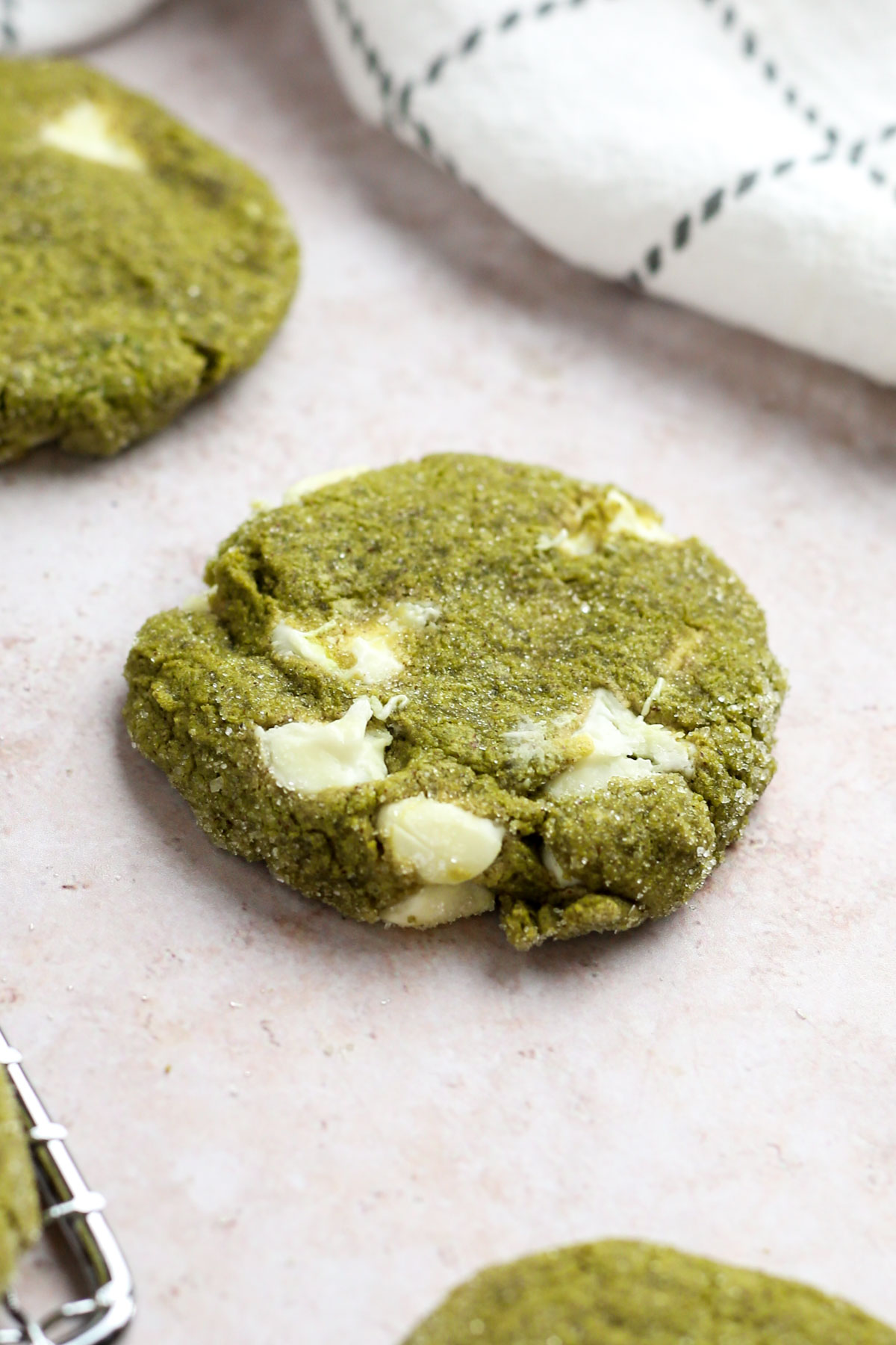 a matcha white chocolate cookie on a table, with sugar glistening on top the cookie.