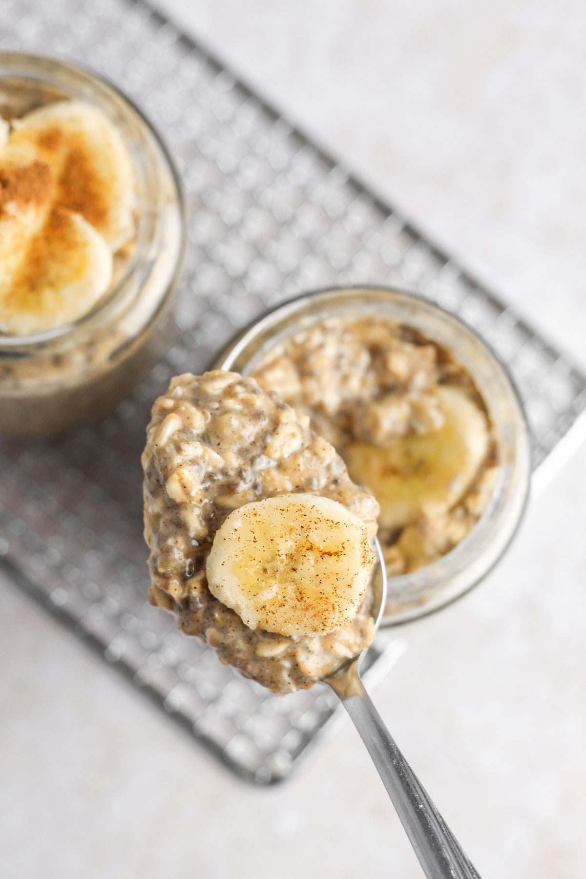 a spoonful of oatmeal with a fresh banana slice on the spoon, and a dash of cinnamon. The spoon is held above a jar of oats.