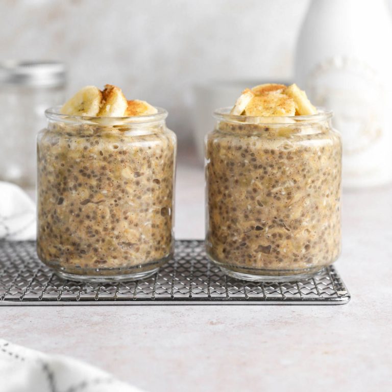 two jars of vegan banana cinnamon overnight oats on a silver tray, with fresh bananas on top.