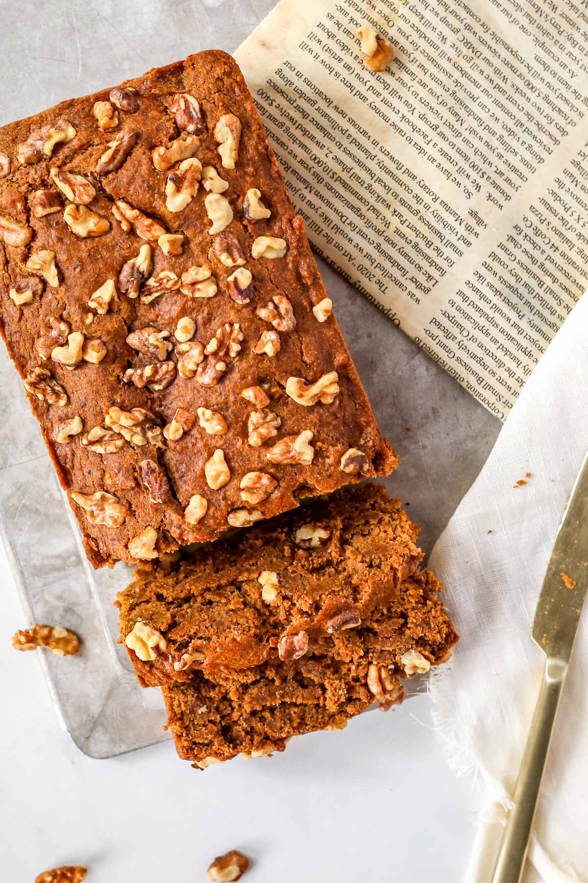 a loaf of pumpkin bread with chopped walnuts on top. The bread is sitting on a gray tray.