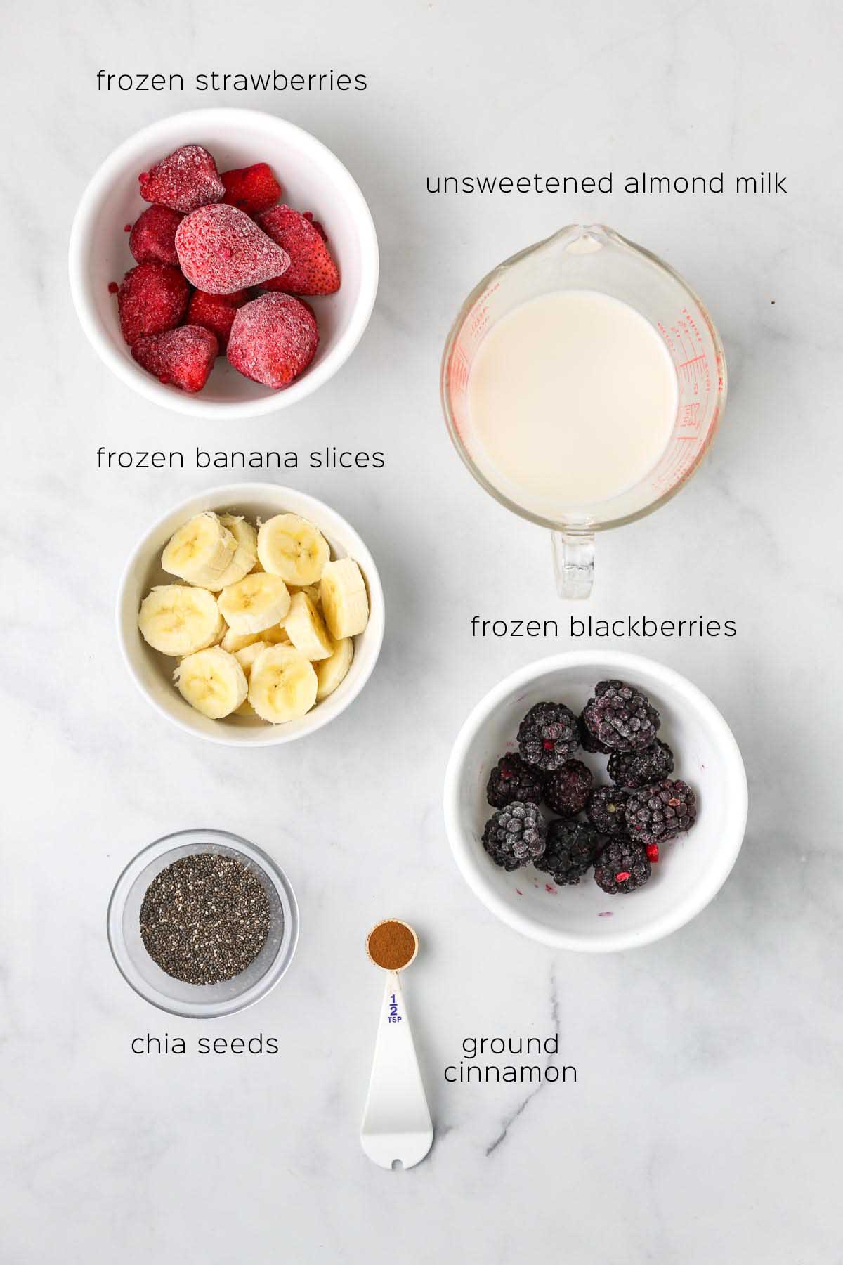 all ingredients to make the smoothie prepared in small bowls and measuring cups on a marble surface.