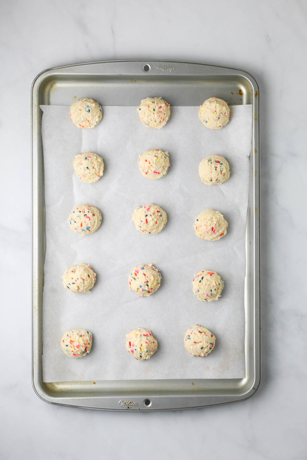 unbaked sugar cookie dough balls placed on a large baking sheet with parchment paper.