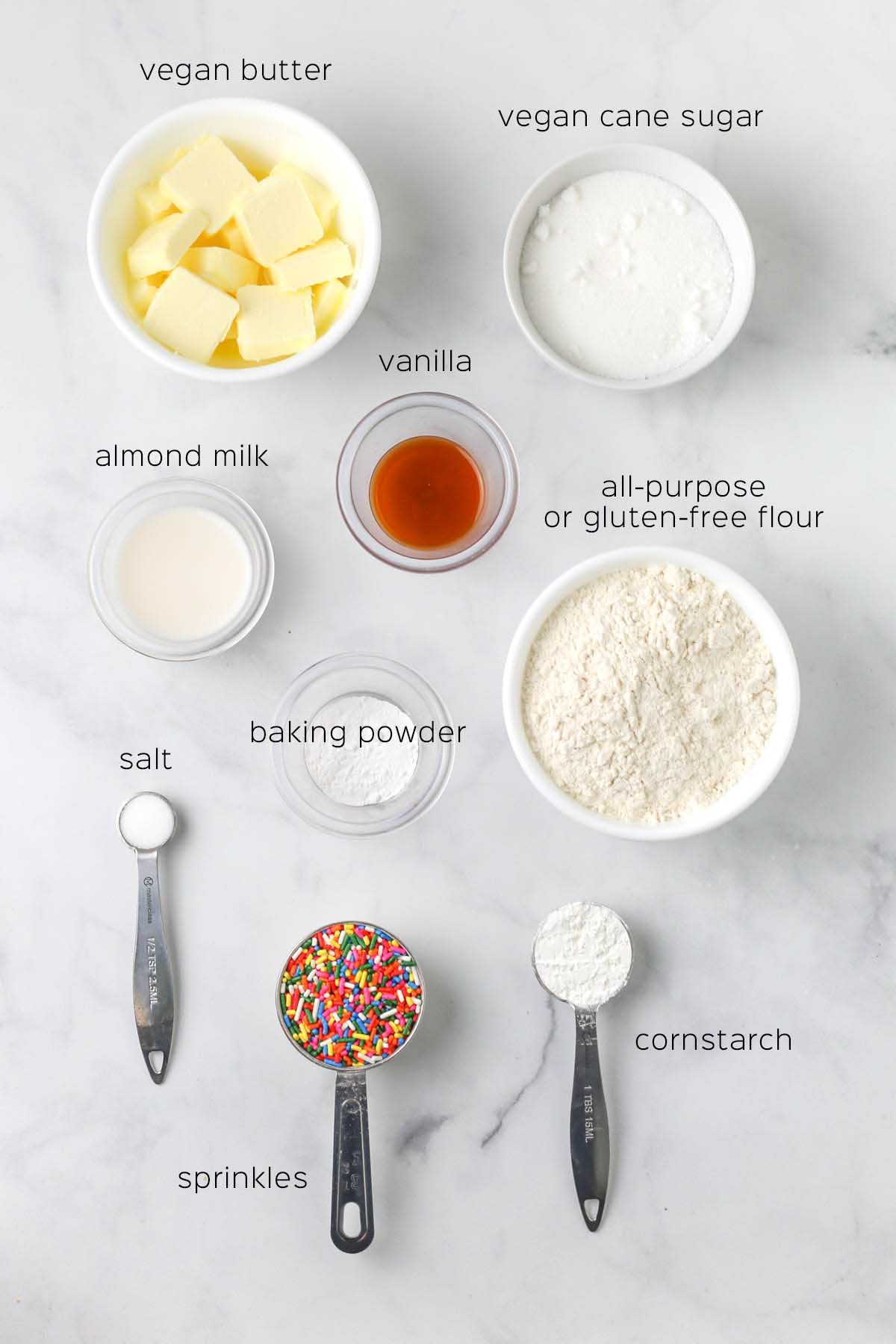 all ingredients to make the cookies prepared in small bowls and measuring cups on a marble surface.