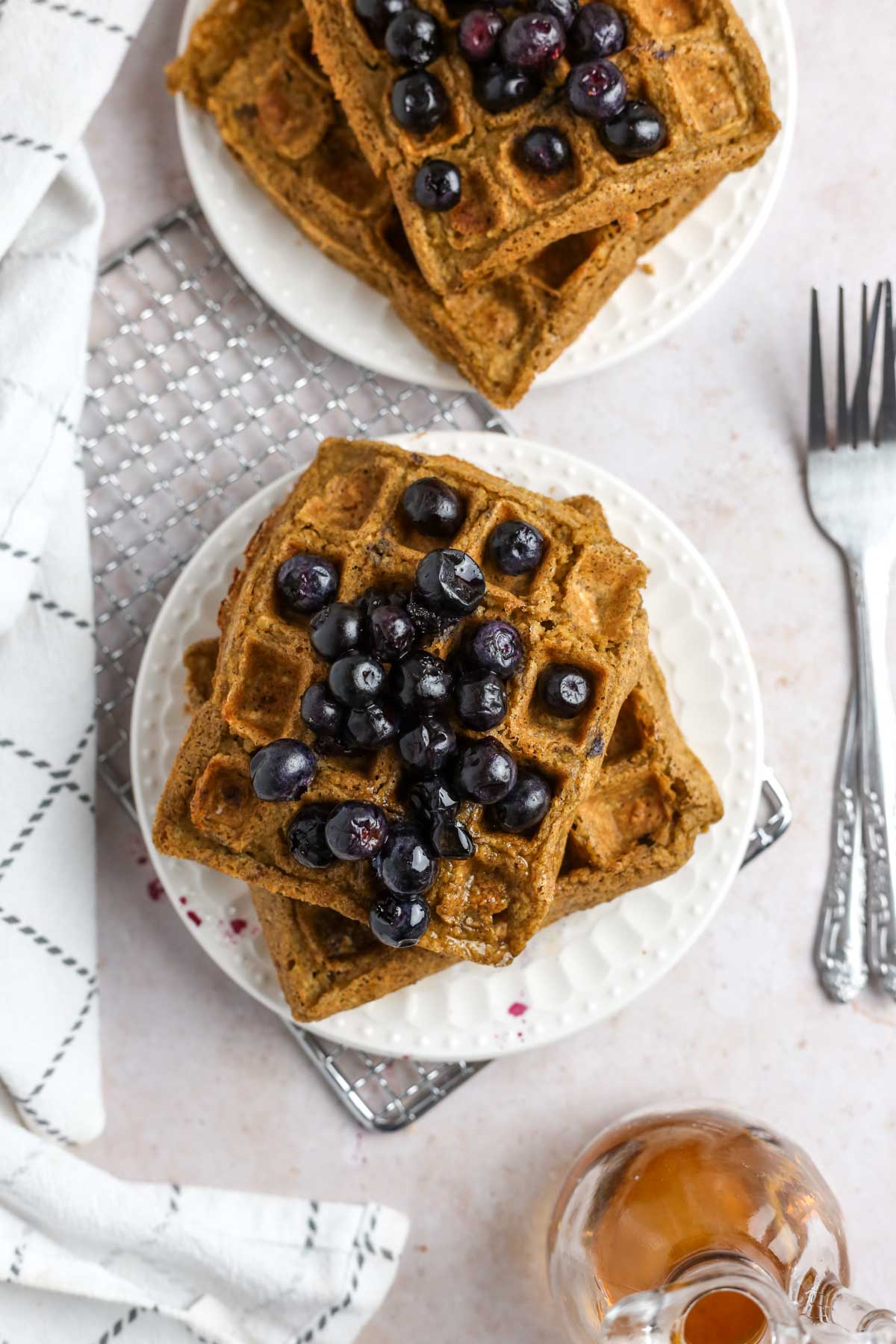 two plates of vegan protein waffles shown from above with fresh blueberries on top.