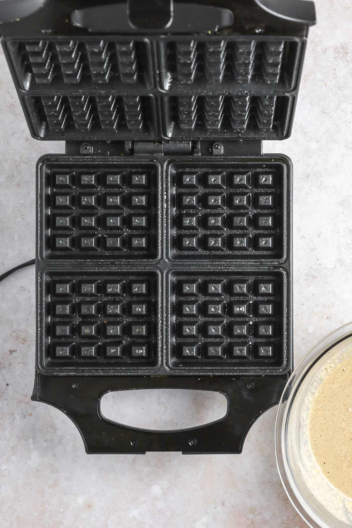a waffle iron heating up and sprayed with non-stick cooking spray.