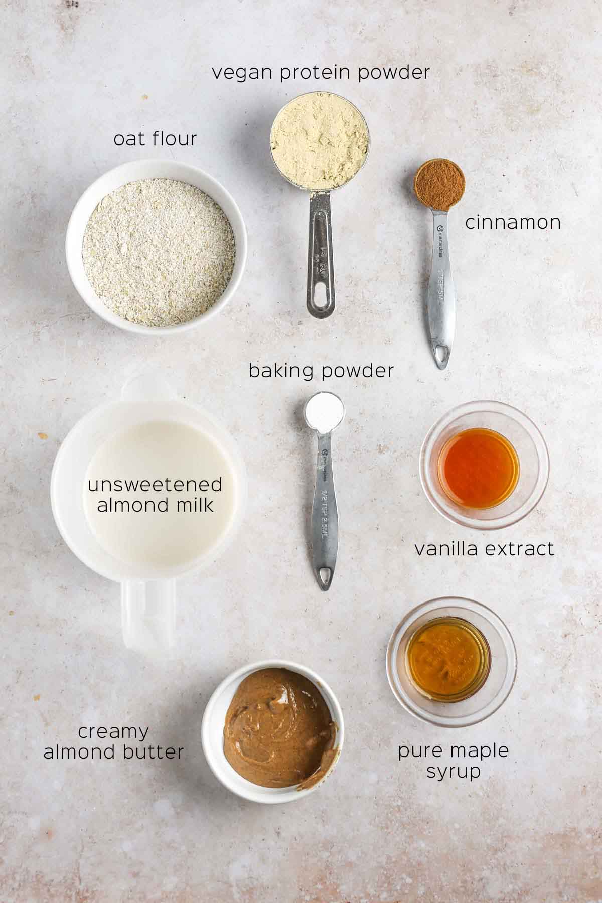 all ingredients to make the waffles prepared in small dishes and measuring cups, shown on a cream marble surface.