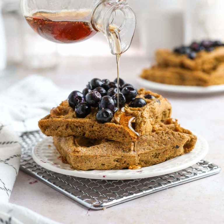 a stack of two vegan protein waffles with fresh blueberries and maple syrup on top.