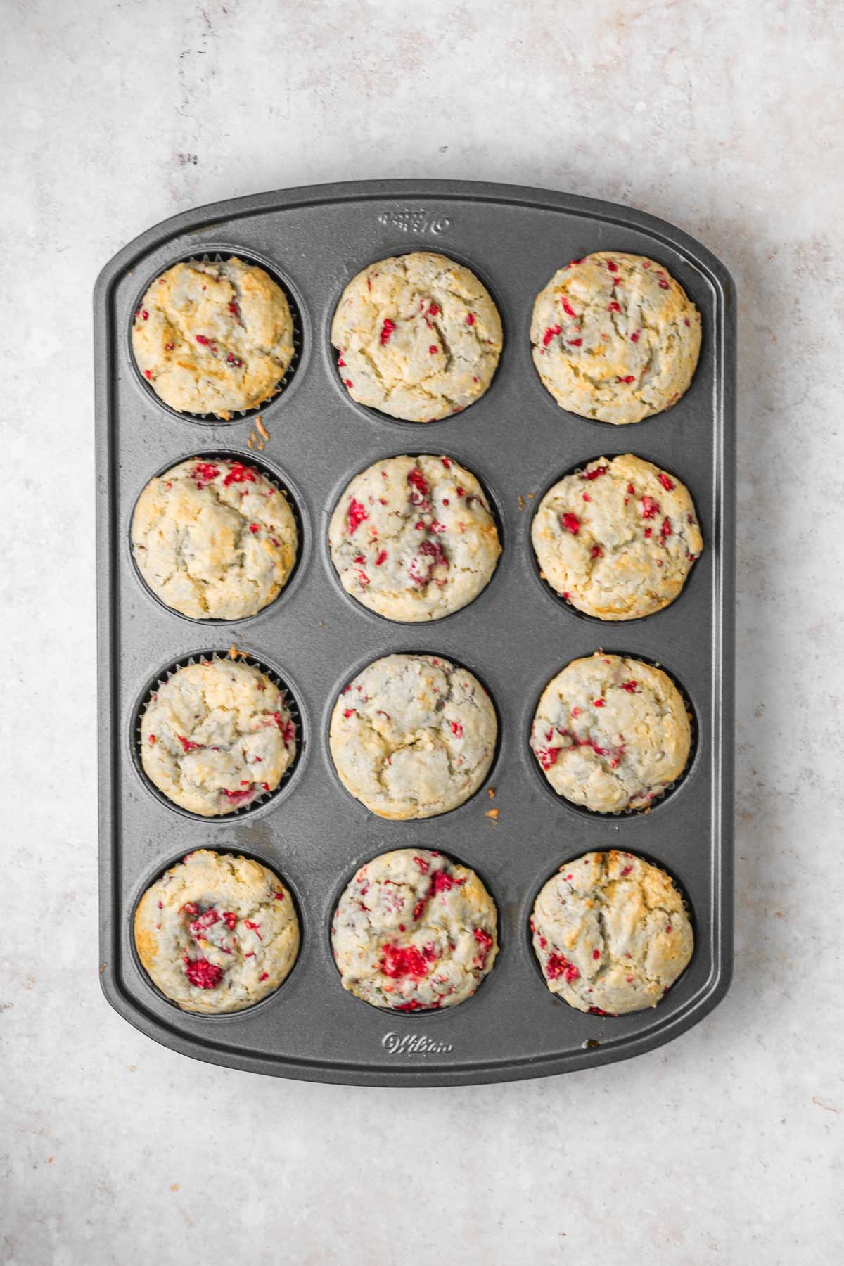 baked raspberry muffins in a gray muffin pan.