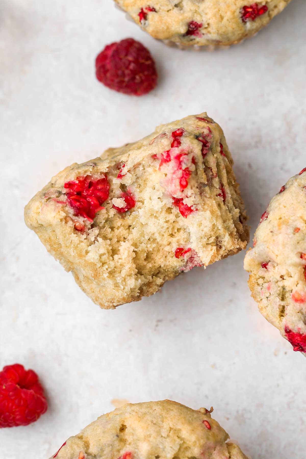 a fluffy healthy vegan raspberry muffin shown from above, with a bite missing from the muffin.