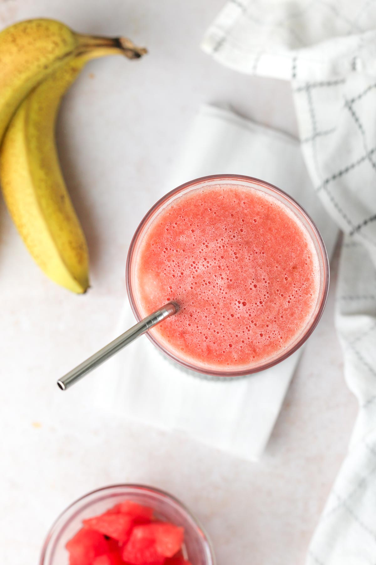 a pink watermelon banana smoothie in a glass, shown from above with a straw.