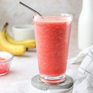 a pink watermelon banana smoothie in a glass with a straw.