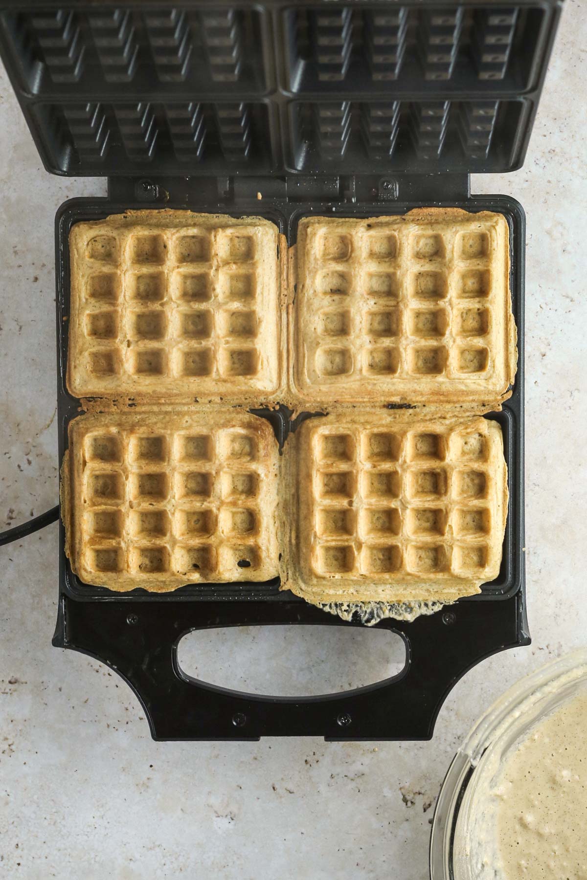 cooked oat flour waffles in the waffle iron before removing them, shown from above. Golden brown in color.