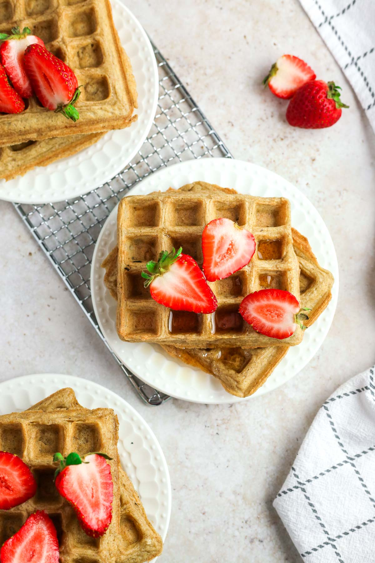 multiple plates of oat flour waffles shown from above, topped with fresh strawberries and maple syrup.