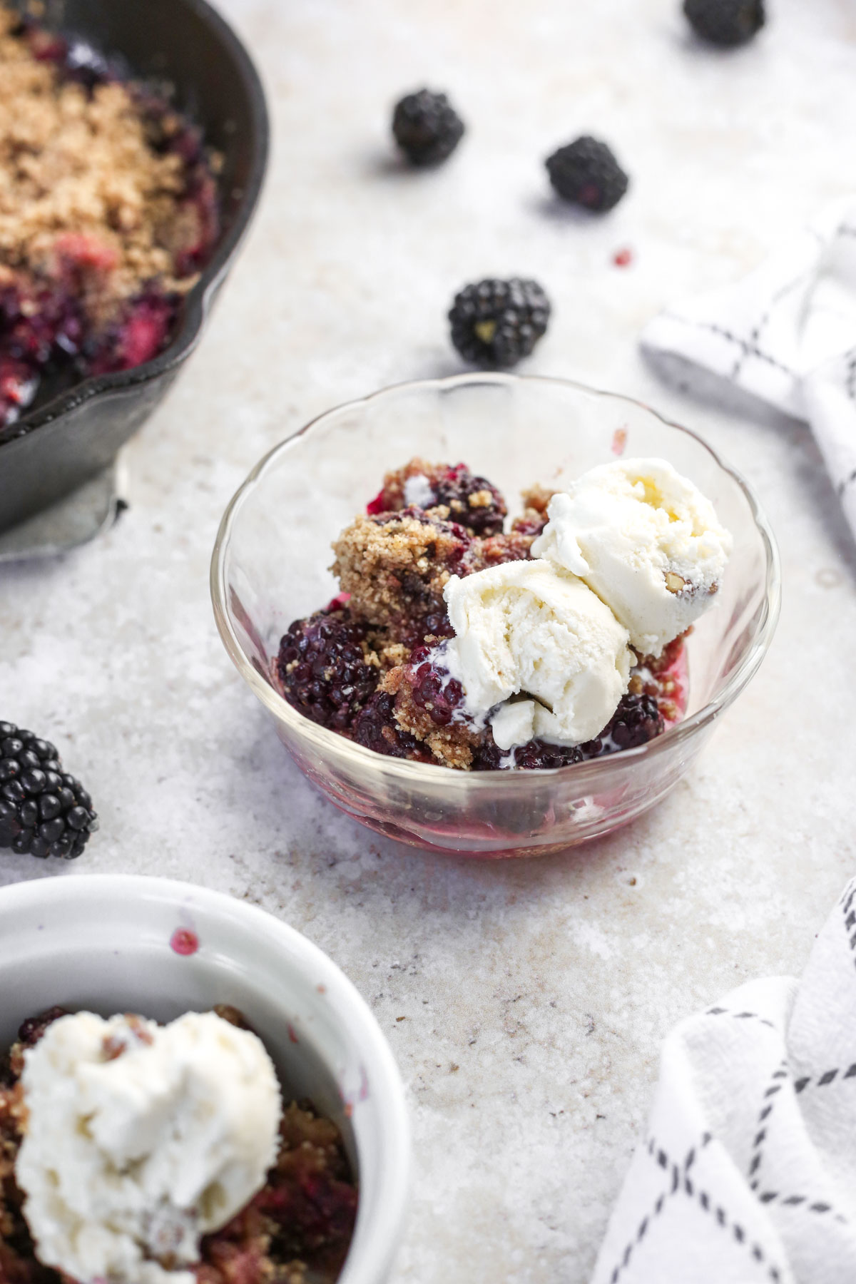 a small clear dish filled with blackberry cobbler and a scoop of vanilla ice cream.