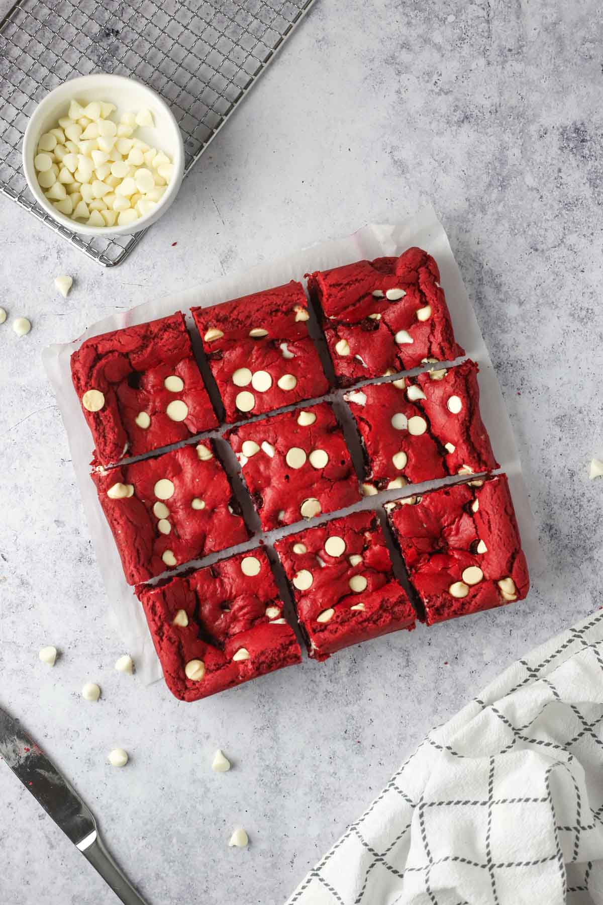 an array of freshly cut red velvet brownies on parchment paper. White chocolate chips surround the scene.