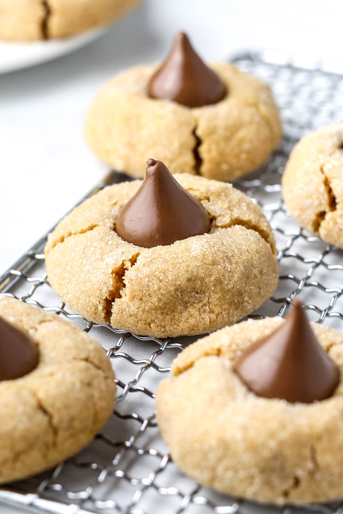 multiple peanut butter blossoms cookies on a wire tray, with glistening chocolate in the center of the cookies.