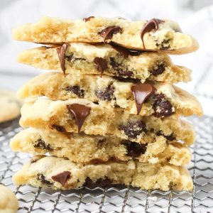 A big stack of chocolate chip cookies without brown sugar on a wire tray. Chocolate chips are melting inside the cookies.