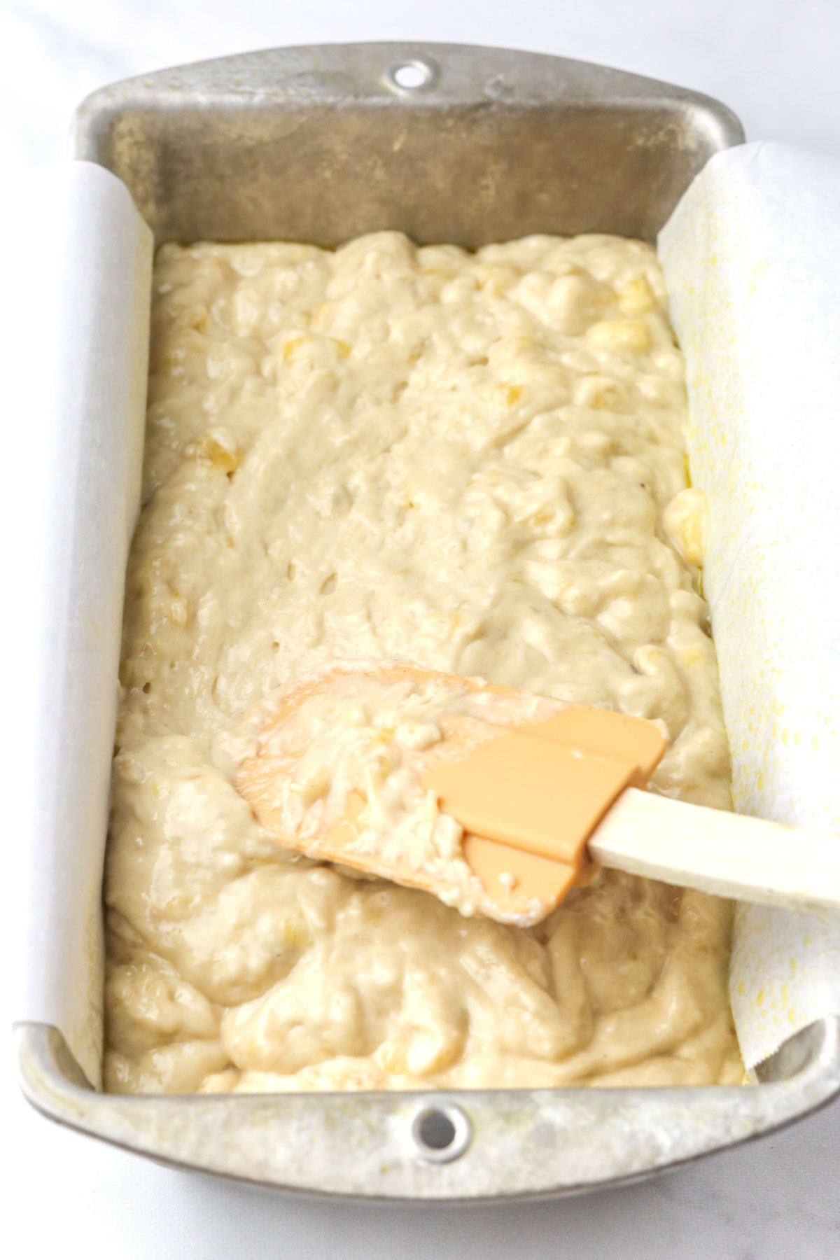 Smoothing the batter into the loaf pan evenly with a rubber spatula.