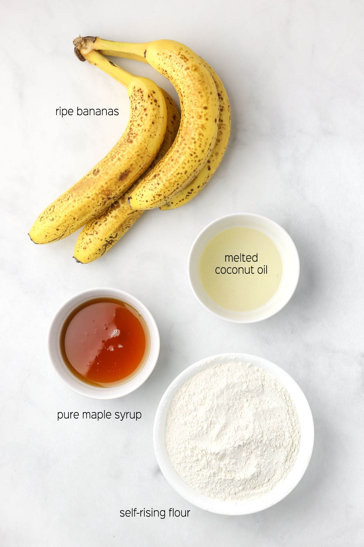 All ingredient to make the banana bread prepared in small dishes on a marble surface.