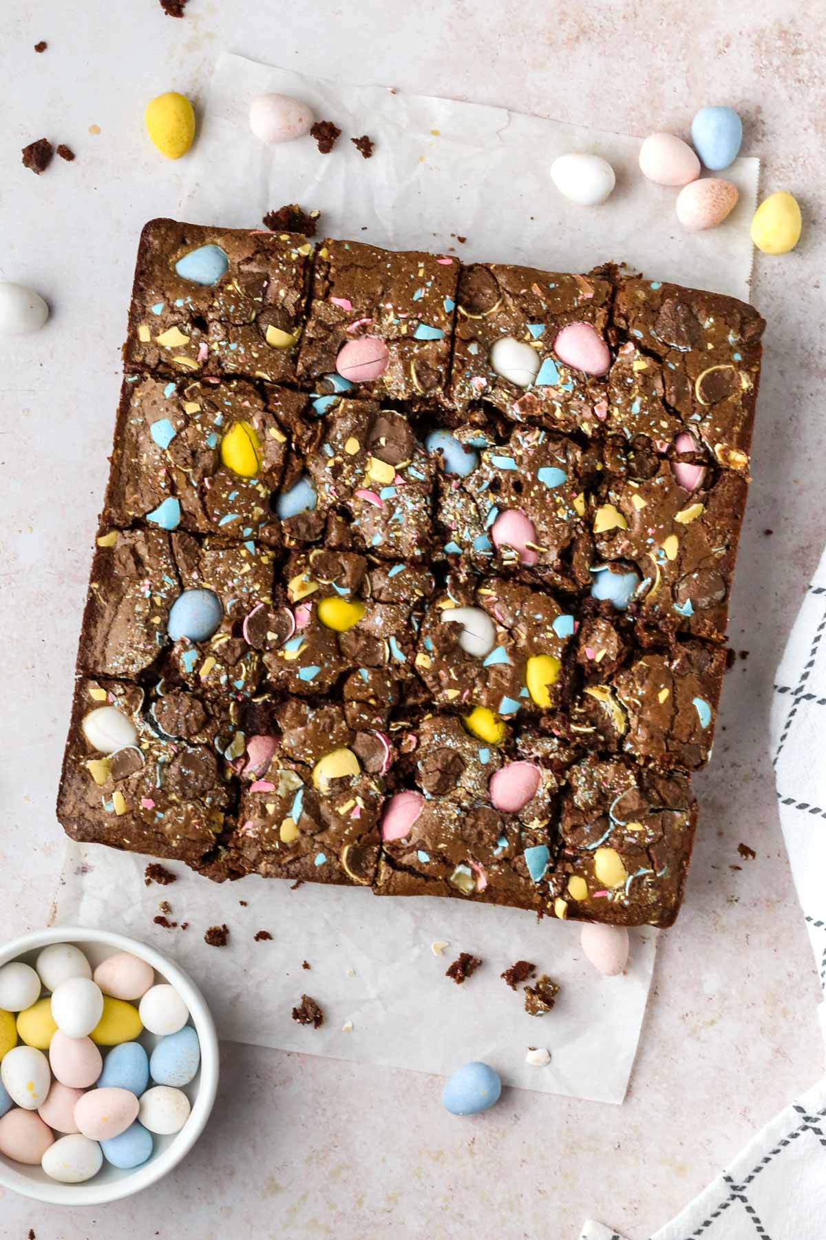 Overhead view of chocolate mini egg brownies sliced into squares on parchment paper.