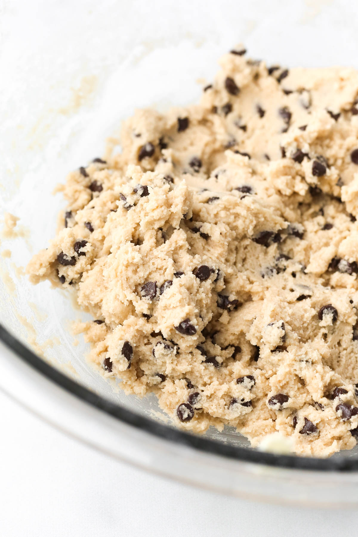 Close-up of no bake chocolate chip cookie dough in a mixing bowl with mini chocolate chips mixed in.