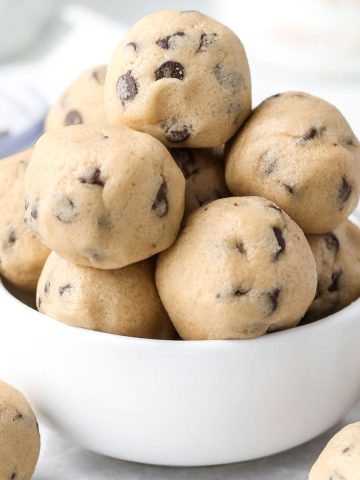 a small white bowl with a dozen small no-bake cookie dough bites in a pile, with chocolate chips inside each ball.