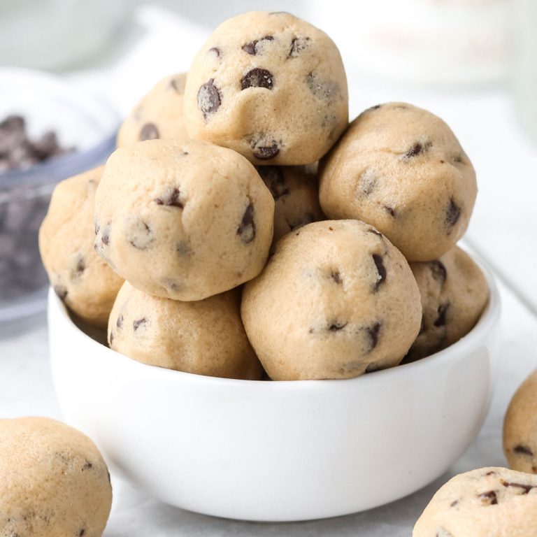 a small white bowl with a dozen small no-bake cookie dough bites in a pile, with chocolate chips inside each ball.