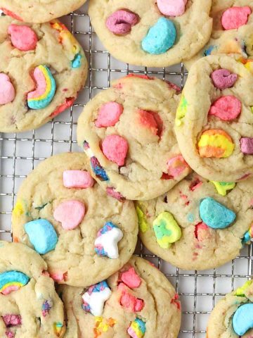 A dozen lucky charms cookies on a wire tray, with lucky charms marshmallows on top.