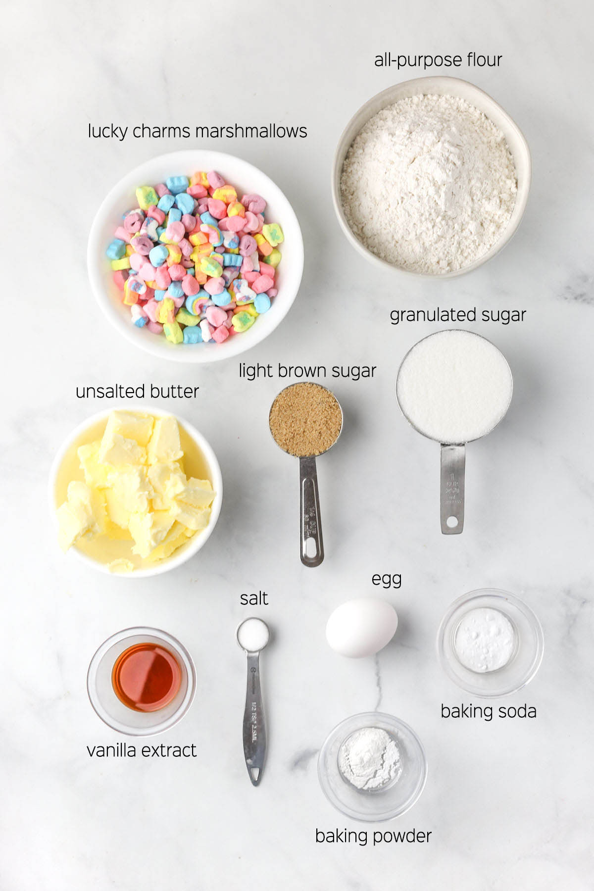 All ingredients to make the lucky charms sugar cookies prepared in small bowls and dishes on a marble surface.
