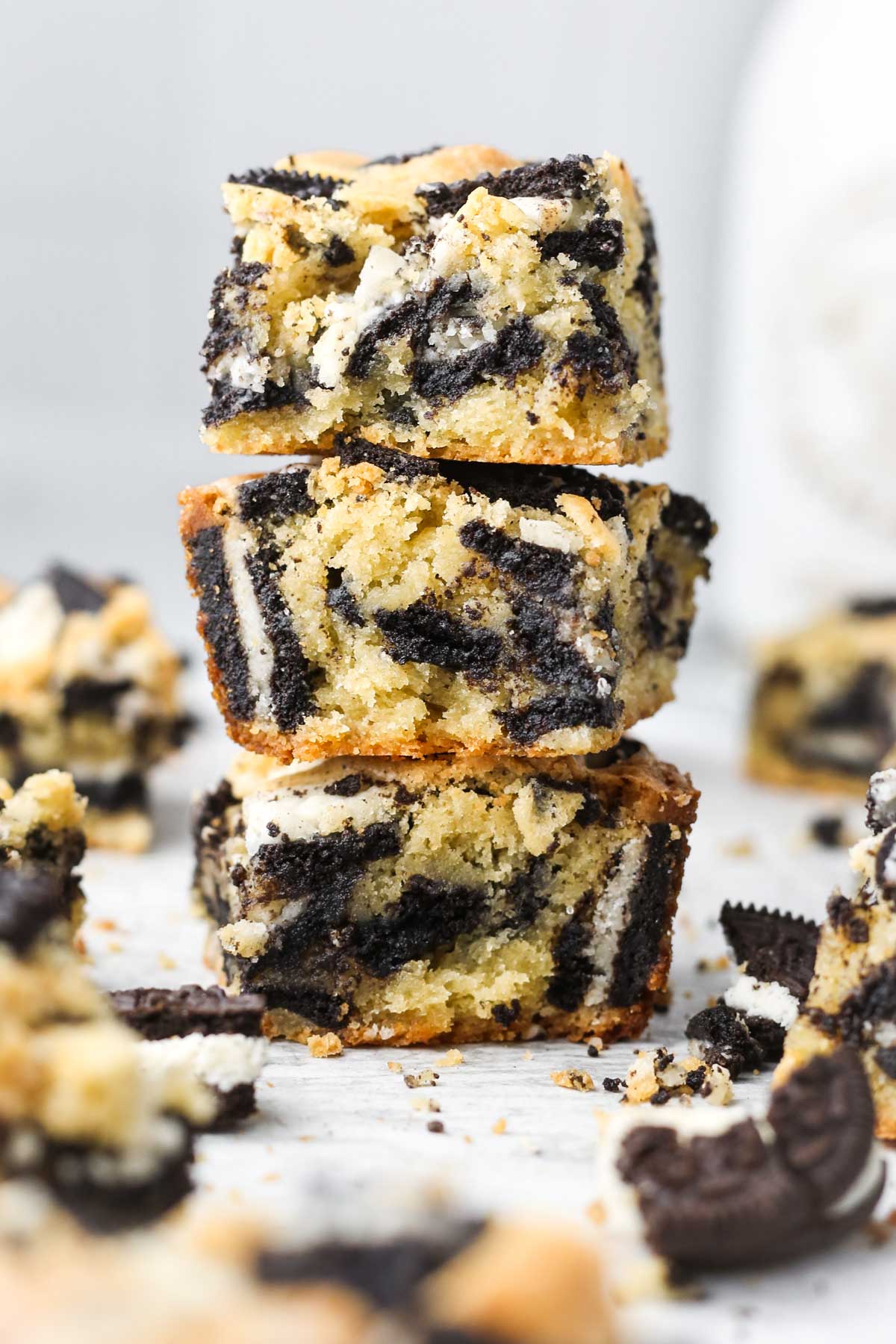 a stack of three thick and fluffy cookies and cream oreo blondies, with oreo cookies shown inside the bars.