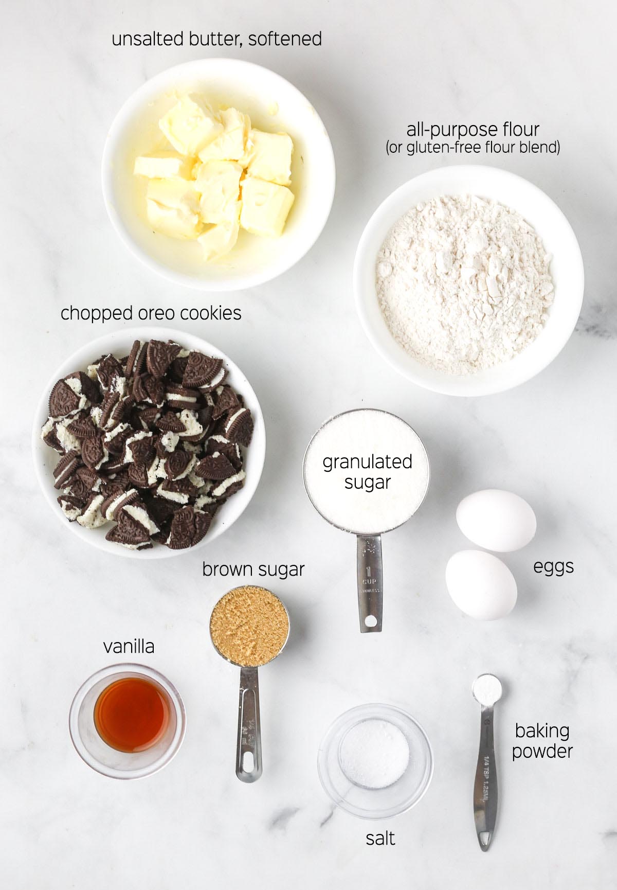 all ingredients to make the blondies prepared in white bowls, shown from on a marble surface.