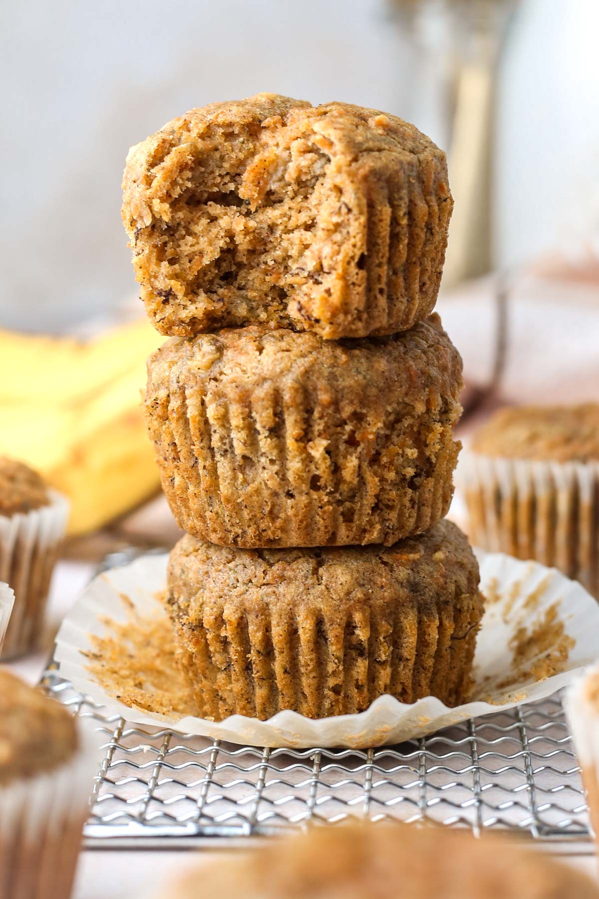 a stack of three healthy carrot banana muffins with the top muffin missing a bite, showing the fluffy texture inside.