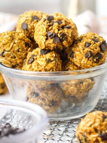 a small clear bowl with multiple pumpkin protein balls inside, full of chocolate chips.