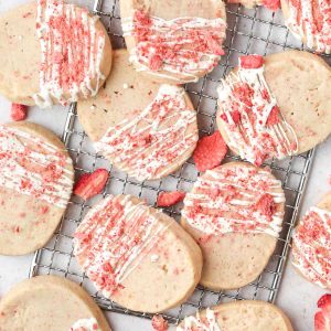 Multiple white chocolate strawberry shortbread cookies shown from above on a wire tray with a drizzle of white chocolate on top.