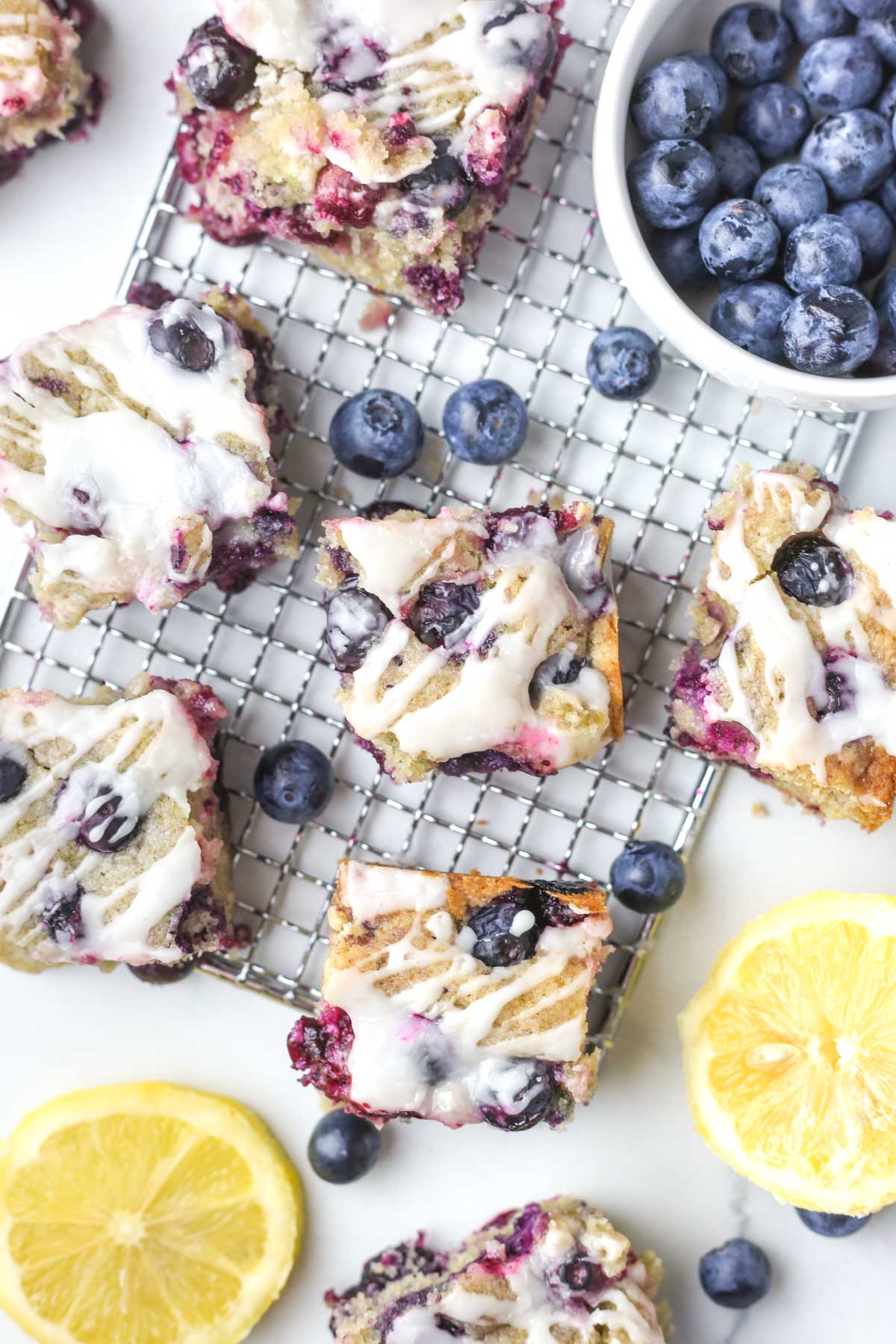 multiple lemon blondies on a tray with fresh blueberries around the scene.