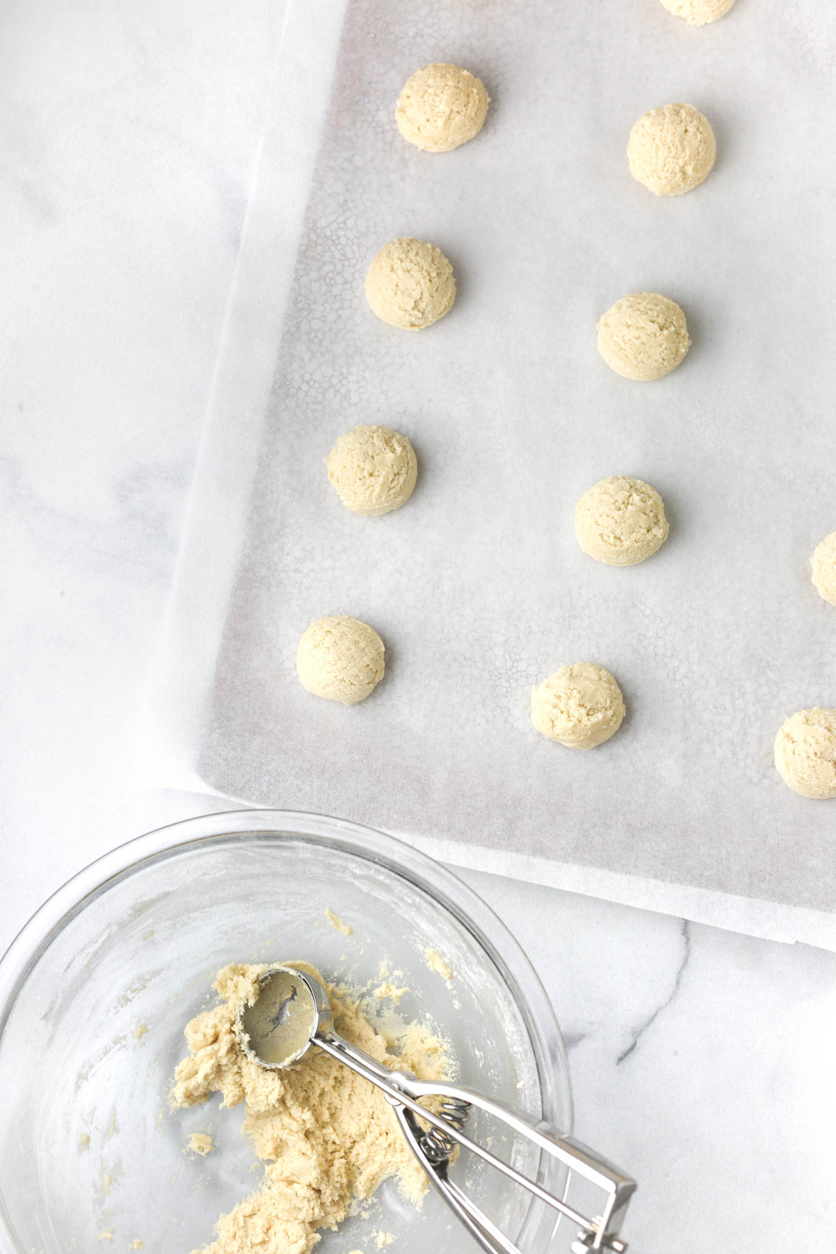 Scooping the cookie dough into balls and placing them on the baking sheet.