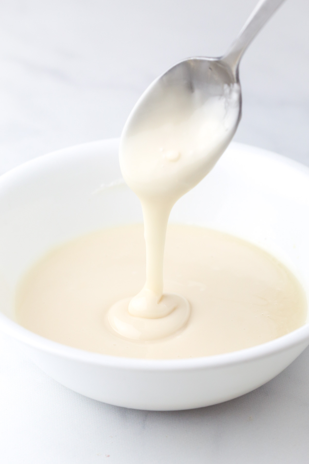 A spoon drizzling thick vanilla icing in a small bowl. 