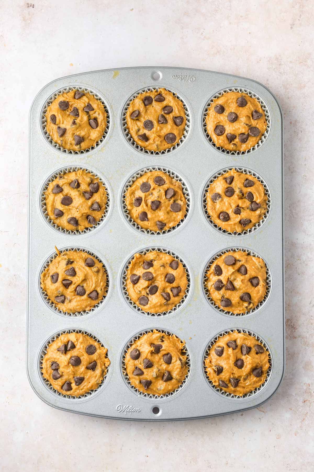 A muffin pan filled with pumpkin muffin batter and chocolate chips on top before baking.